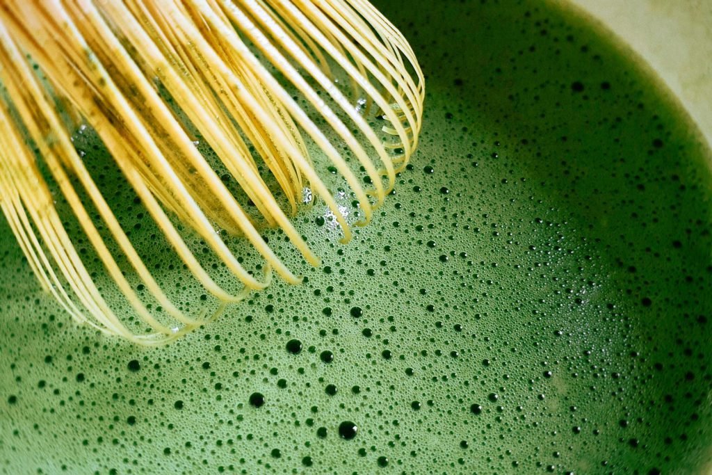 A bamboo chasen whisking matcha in a bowl